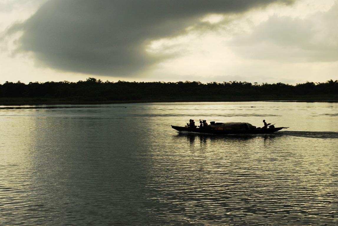 Boats crossing a wide river beneath a dramatic sunset sky