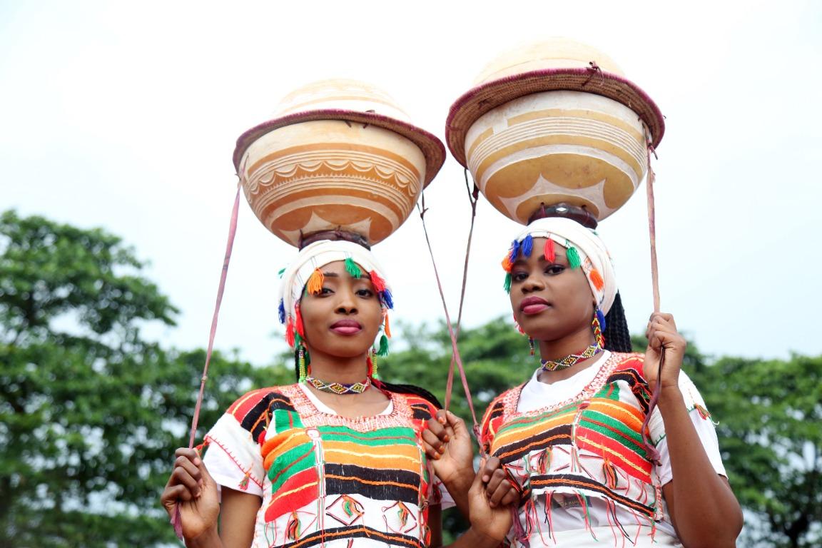Two women in traditional dress carrying decorated vessels